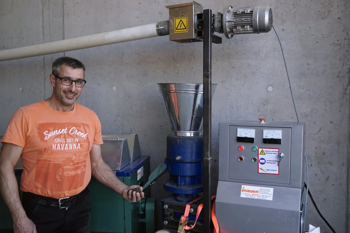 fcb7d94fe574ff70d0c0b0cca366c2dd2ea106d1 Legehennen-Halter Ruedi Huber mit Pellets in der Hand vor der Pelletier- und Trocknungsmaschine. Bild: Michael Götz
