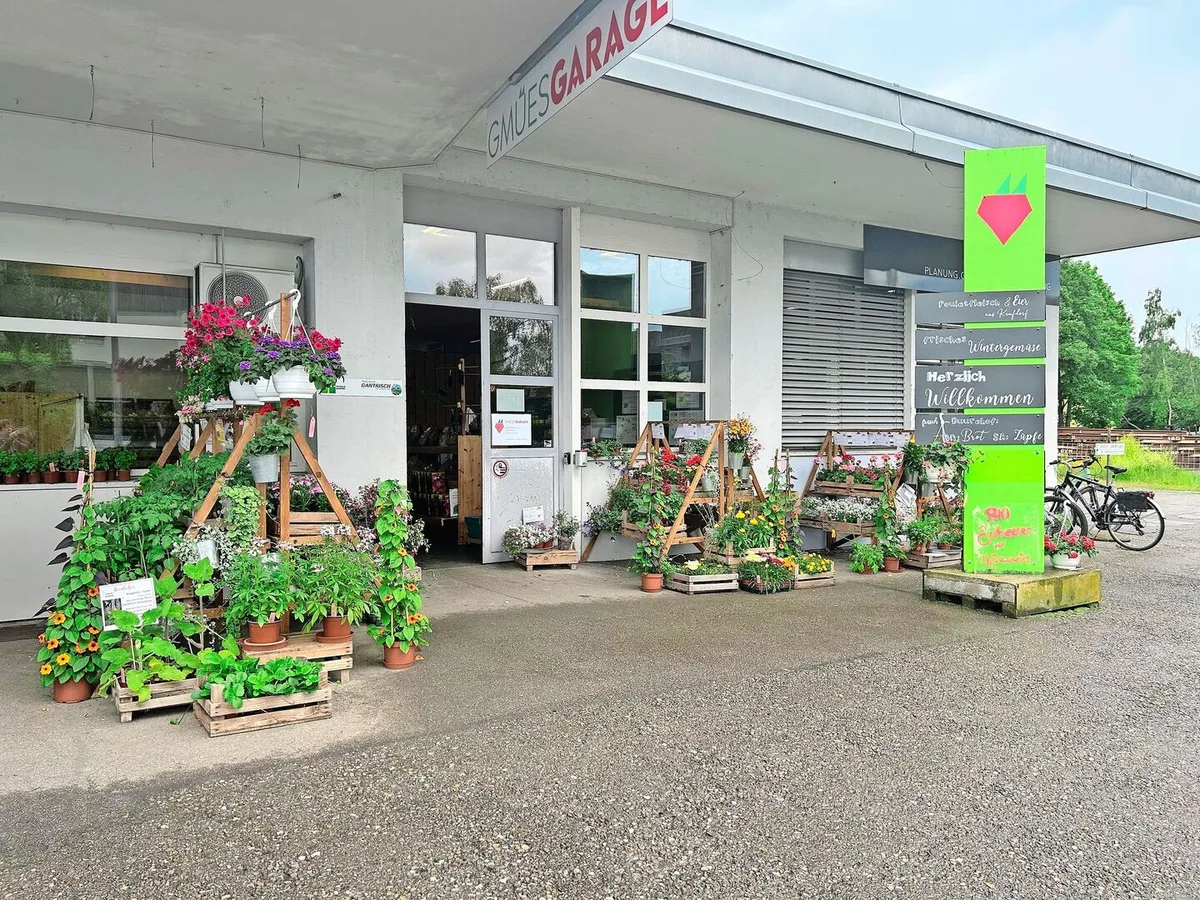 7ed2a747277429f5d6d63b0185770b852ce2376d9790eeab3e3d3342484c51f2 Im Eingangsbereich stehen Blumen und Setzlinge zum Verkauf. Trotz des Schildes erinnert der Hofladen an seine frühere Bestimmung als Garage. Von Vorteil ist die grosszügig bemessene Parkplatzzone.