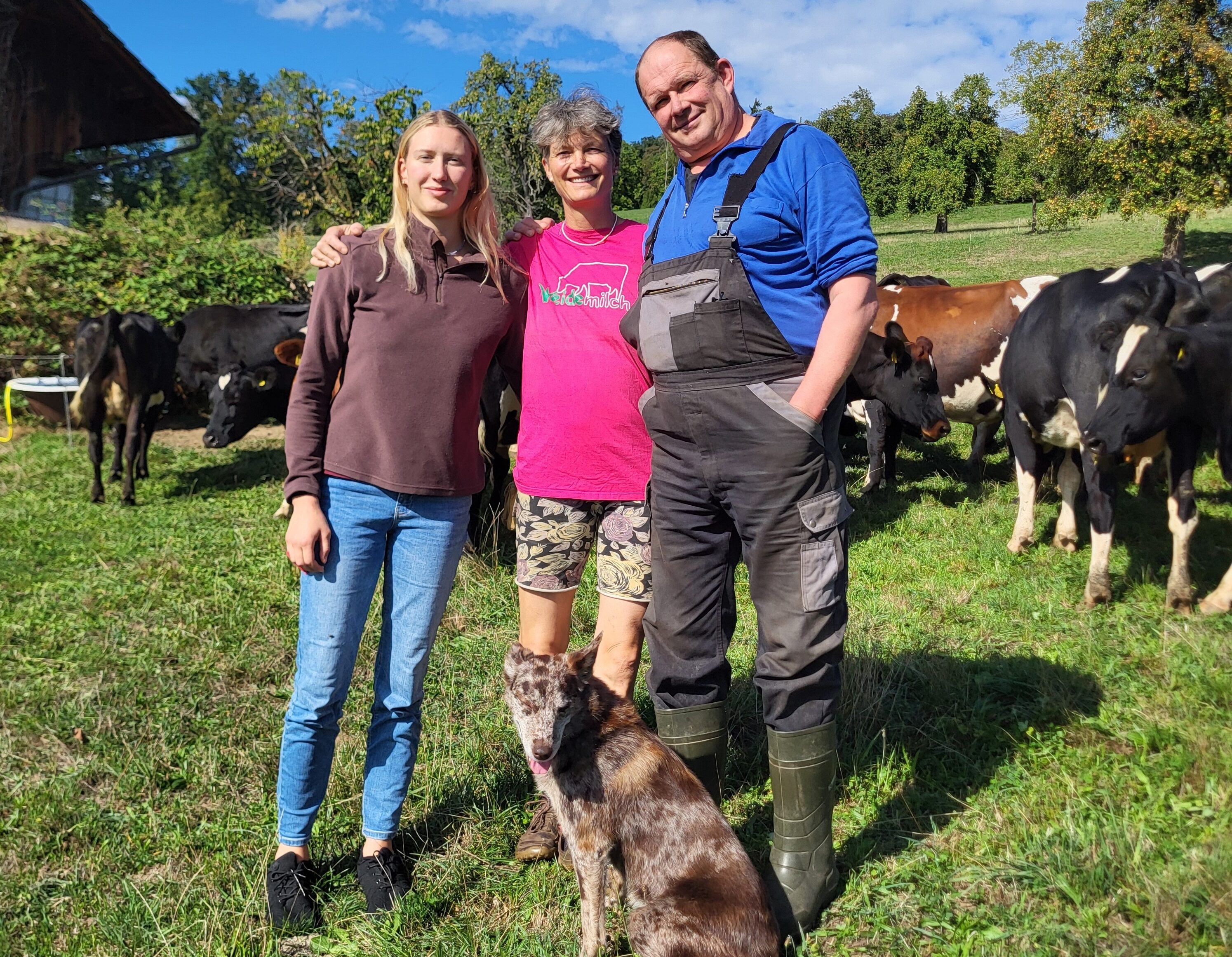 Selina, Helen und Christian Gyr mit der Hündin Leila vor ihrer Weidemilch-Kuhherde. Leila hilft als Treibhund beim Umtrieb der Kühe von einer Weide zur anderen.
