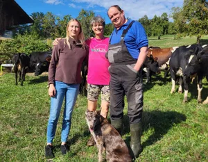 Selina, Helen und Christian Gyr mit der Hündin Leila vor ihrer Weidemilch-Kuhherde. Leila hilft als Treibhund beim Umtrieb der Kühe von einer Weide zur anderen.