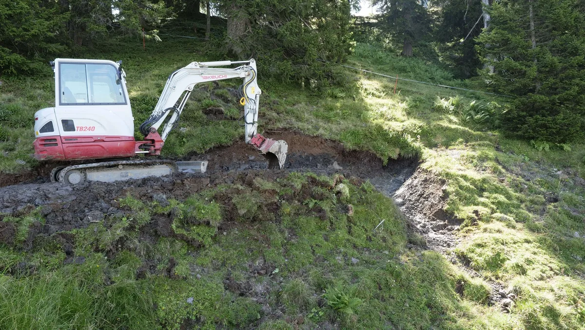 DG_22-10_MM7_Aufmacher Ein Bagger steht im Hang, daneben gluckert ein kleines Wasserrinnsal hinunter.