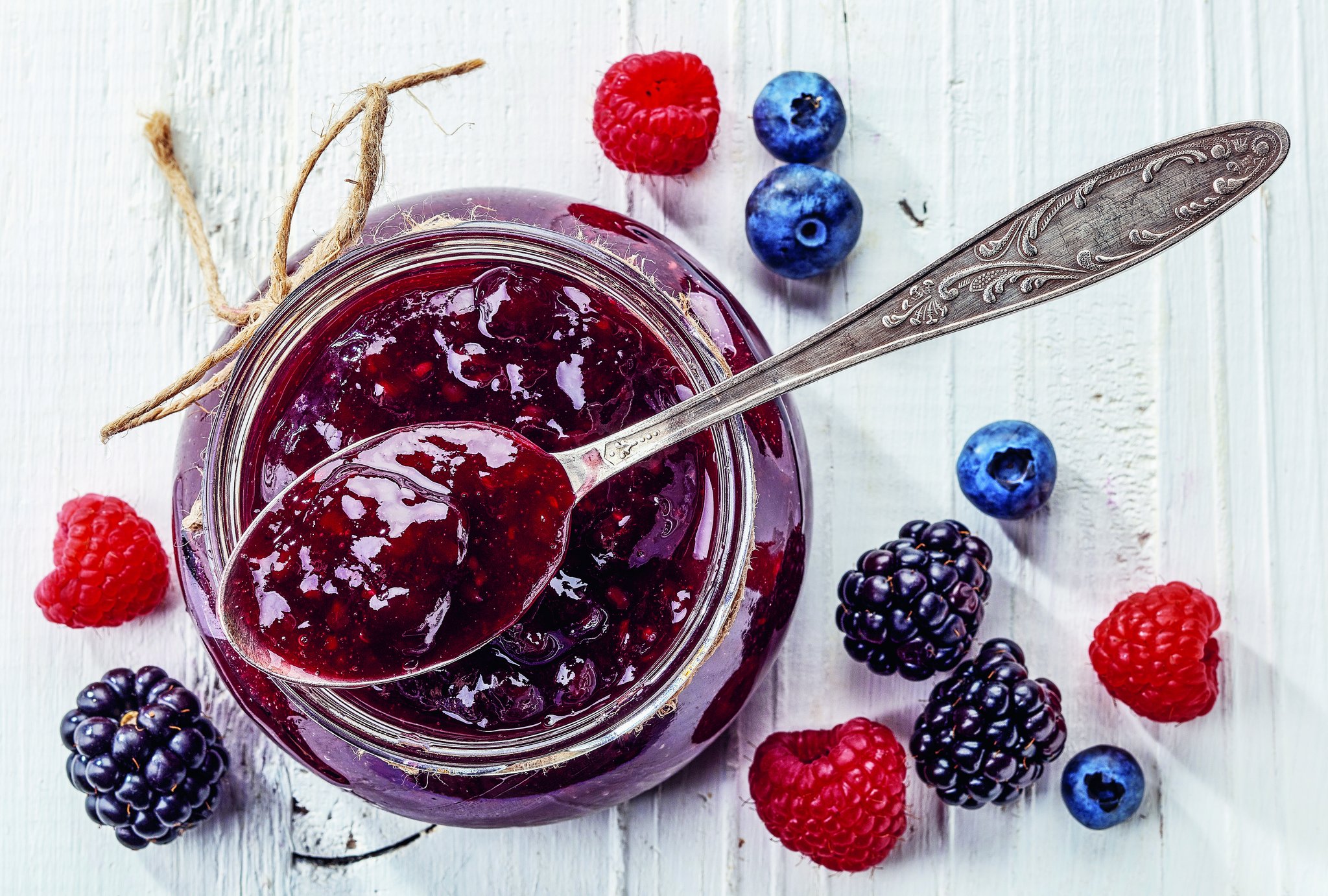 Himbeeren, Brombeeren und Heideleeren neben einem Glas Konfitüre.