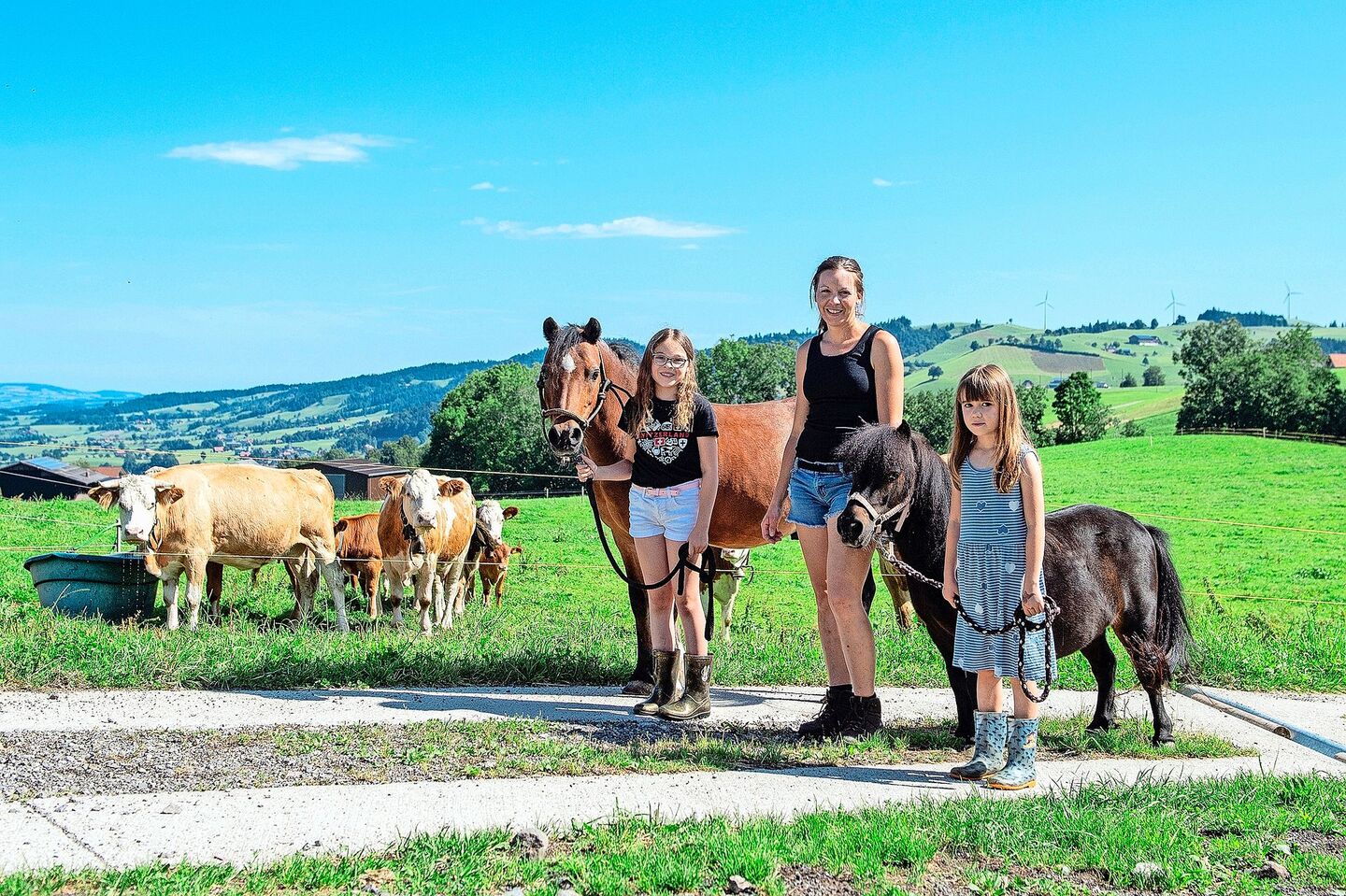 Larissa mit ihrem Pony Dino, Martina Wicki und Lea mit dem Shetty Leni. Die betriebseigenen Simmentaler-Mutterkühe mit ihren Kälbern beobachten die Szene.