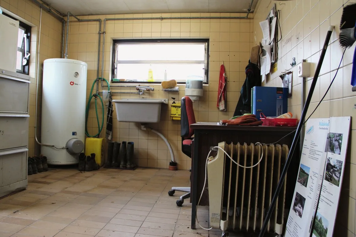 Die Arbeitsschuhe trocknen in dieser einfachen Schmutzschleuse unter einem Trog, ein Elektro-Ofen spendet etwas Wärme.Der Nassraum wird auch als Abstellraum genutzt – als Arbeitsplatz für andere Tätigkeiten eignet er sich hingegen nicht.