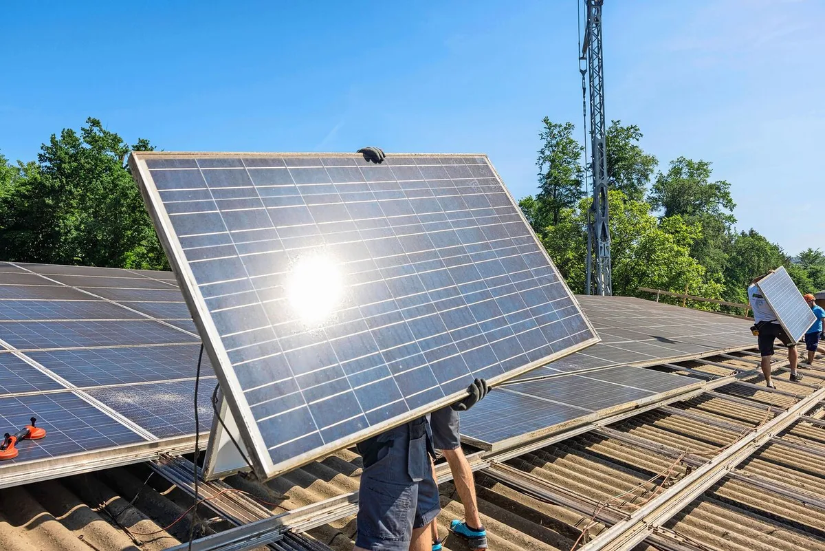 3bffb7b70d00277faa0513be981806d2fbf860de662c3e03a143822c953963b4 Ein Monteur trägt ein Solar-Panel, das er auf dem Dach montieren will.