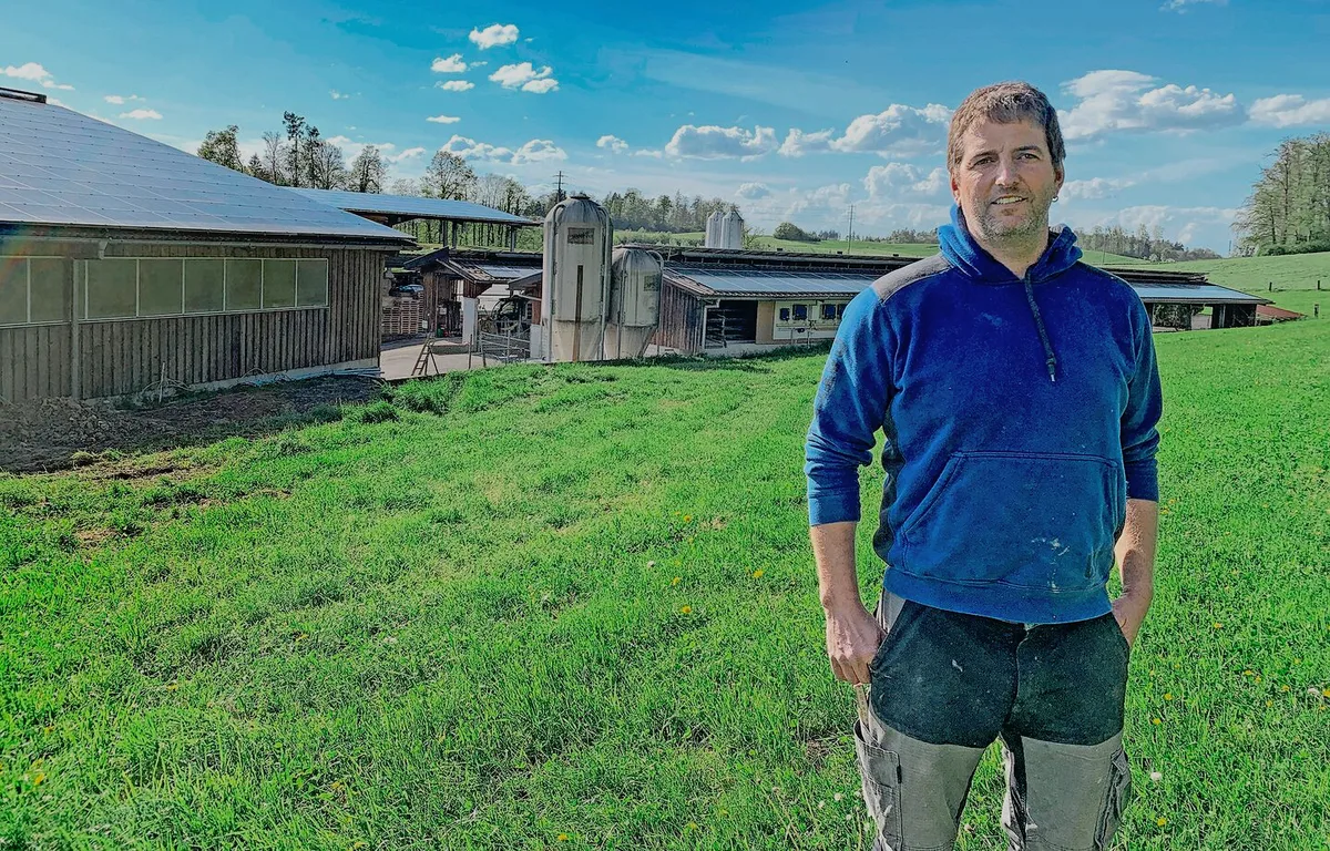 ______rgbchange_01 Philipp Boss von der Büelweid in Knonau vor den Gebäuden mit PV-Anlagen. Links die Maschinenhalle, rechts die Milchviehscheune, hinten die überdachten Fahrsilos. Nicht sichtbar ist die ebenfalls mit PV-Modulen belegte Geflügelmasthalle.