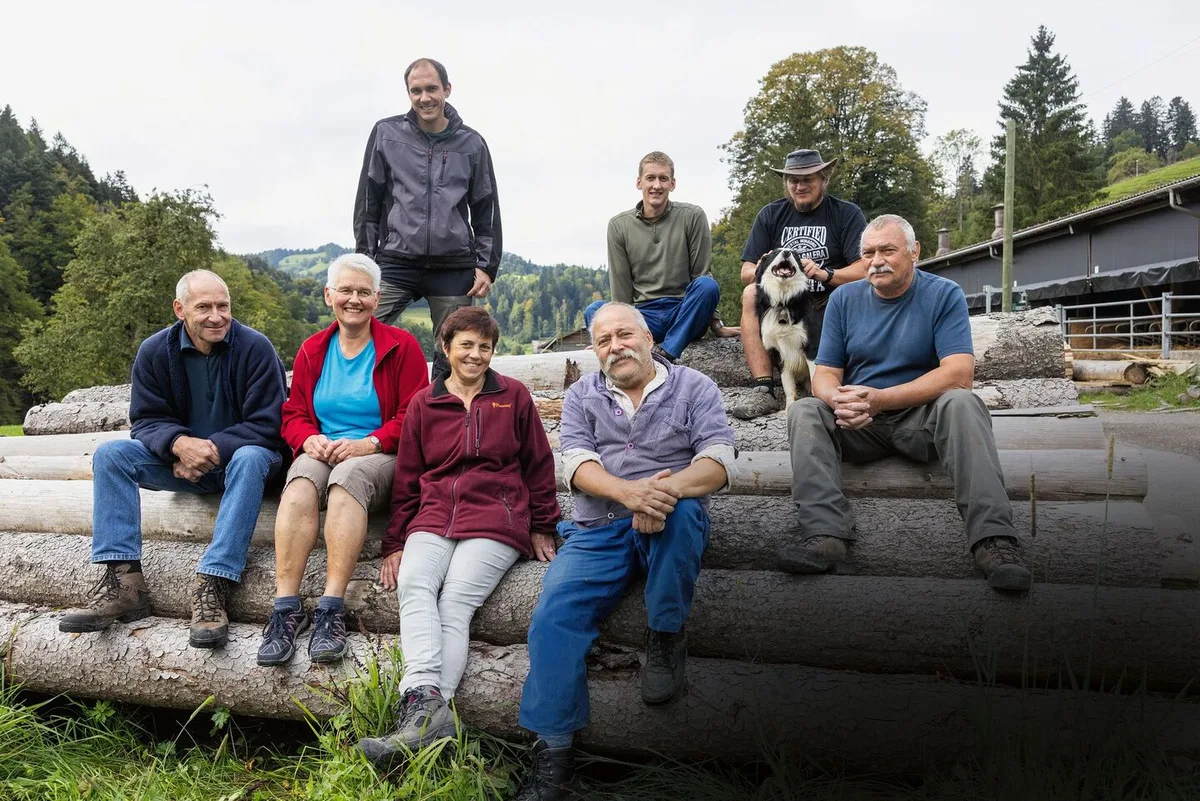 caad006eba18a3f714bce04e8d8b409c36b14dc2e6b191c4863b3be5754d3e16 Gruppenbild der drei Familien, wie sie auf Holzstämmen sitzen.