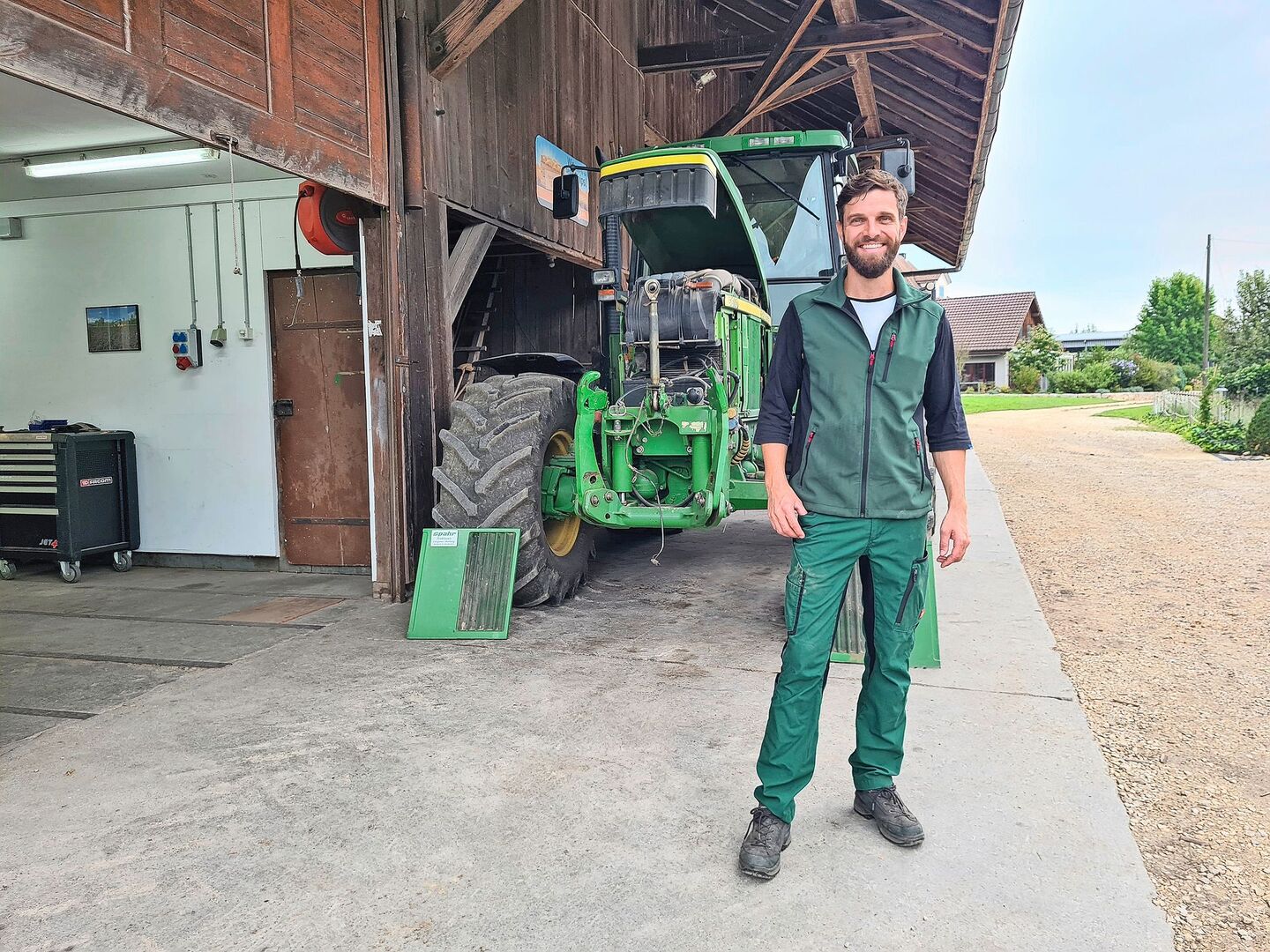 Lukas Streit steht auf dem Hofplatz, vor dem Traktor.