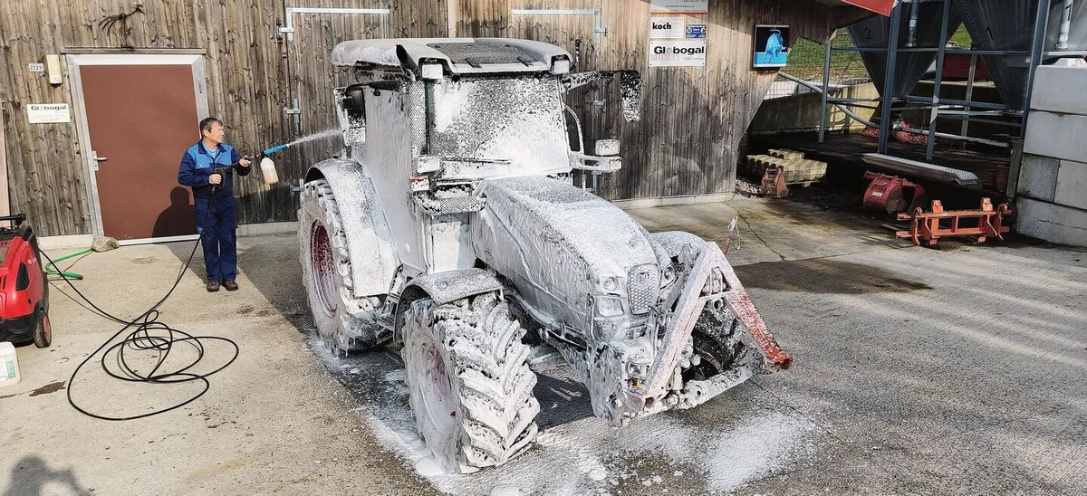 Ein Mann sprüht den Traktor mit weissem Schaum voll.