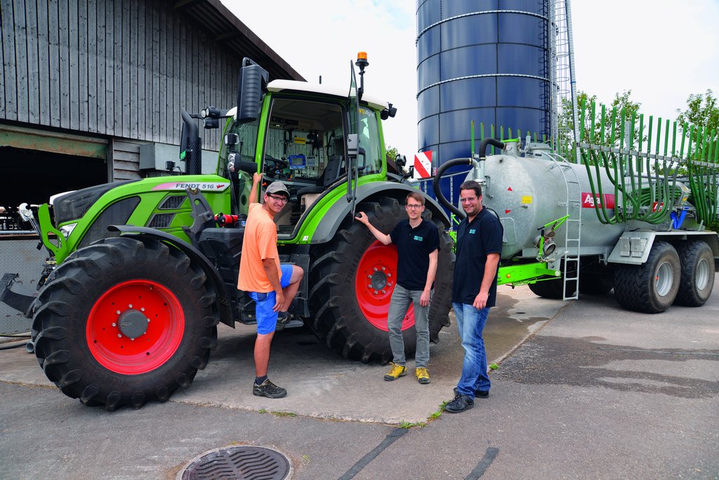 Flavio Näf (links), Florian Abt (Mitte) und Marco Landis (rechts) von der Swiss Future Farm stehen vor dem Traktor, an dem ein Güllefass angehängt ist.