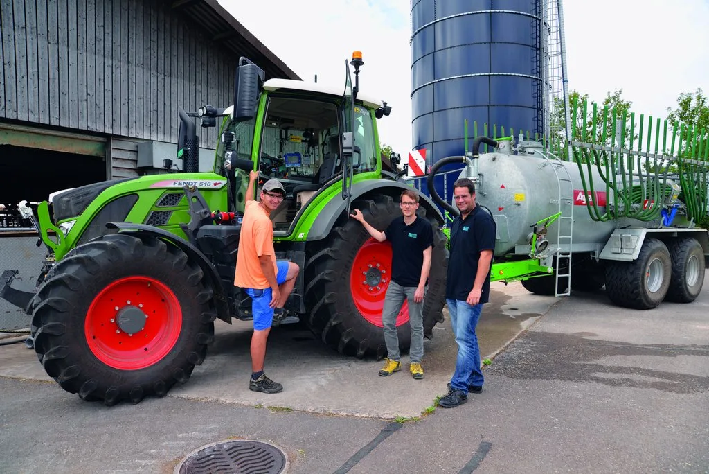 Flavio Näf (links), Florian Abt (Mitte) und Marco Landis (rechts) von der Swiss Future Farm stehen vor dem Traktor, an dem ein Güllefass angehängt ist.