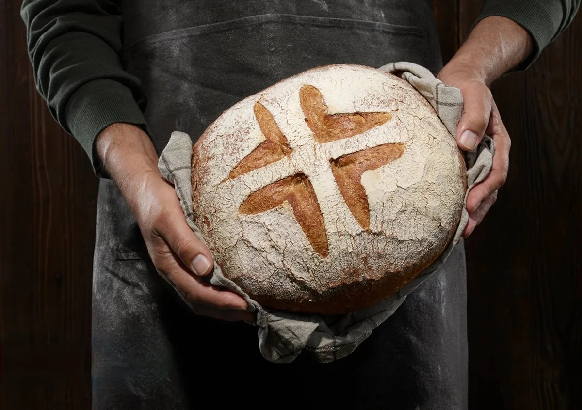 schweizer_brot_logo Ein Bäcker hält einen Brotlaib mit dem Schweizer-Brot-Logo in den Händen.