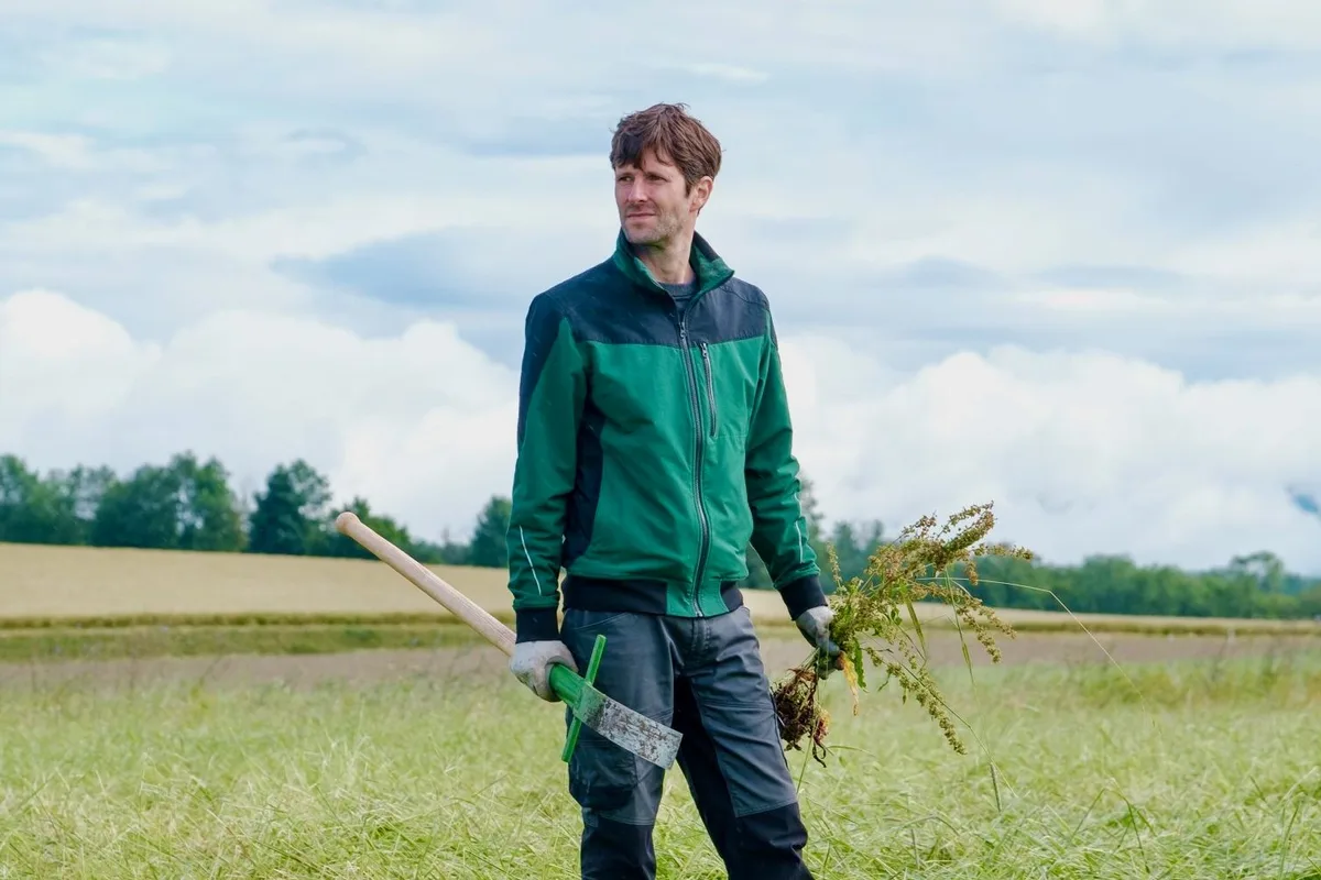 baumann-kilian_feldarbeit Kilian Baumann steht in Arbeitskleidung auf einem Feld.
