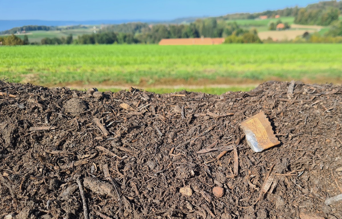 An einer Kompostmiete am Feldrand sind diverse Verpackungen und Fitzelchen von Plastik zu sehen.